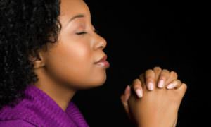 Black woman in  purple top praying