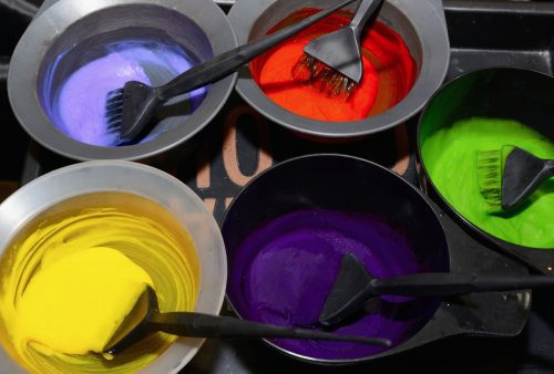 Many different colors of hair dye in bowls with brushes.