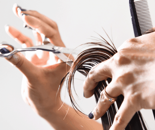 Closeup of hands holding comb and cutting hair with shears.