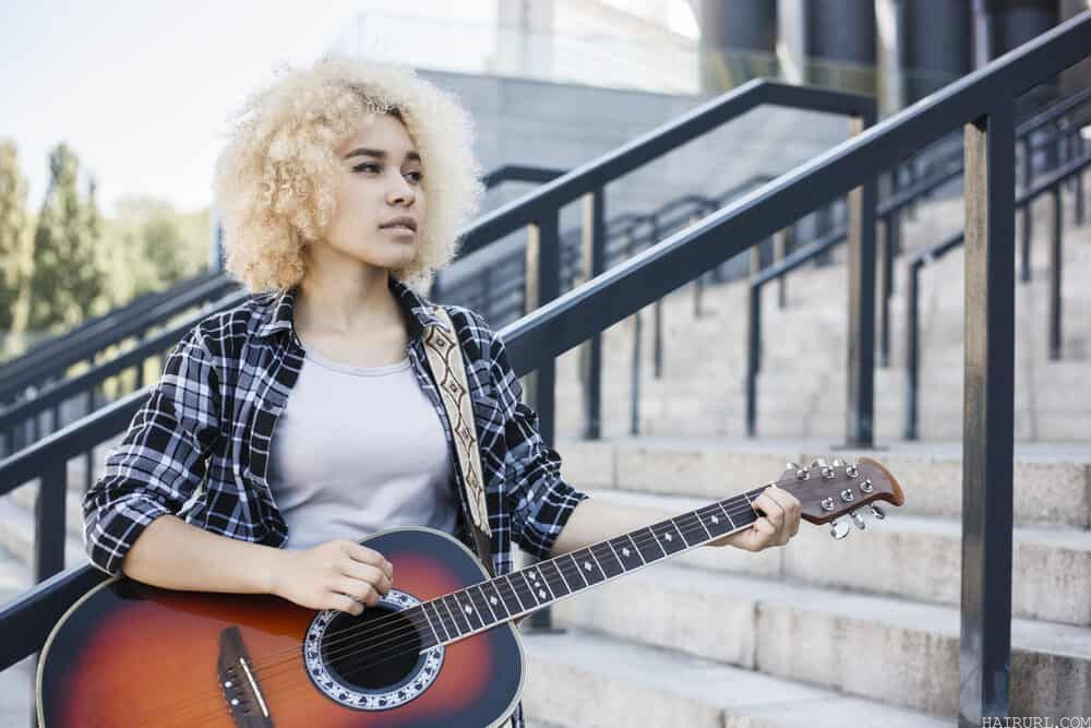 Beautiful young black lady playing the guitar with ash blonde hair dye covering her natural dark hair
