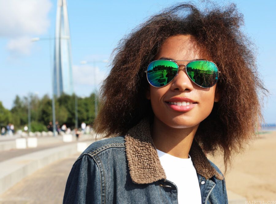African American female with thick hair sticking up wearing sunglasses and a blue jean jacket.