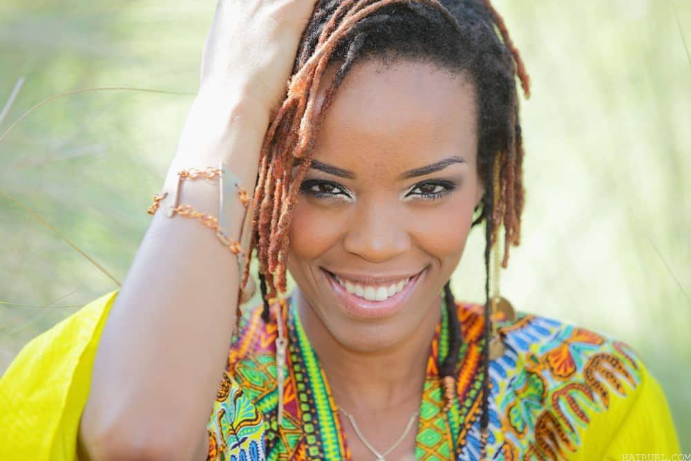 African female wearing a multi-colored shawl holding her 4C natural hair.
