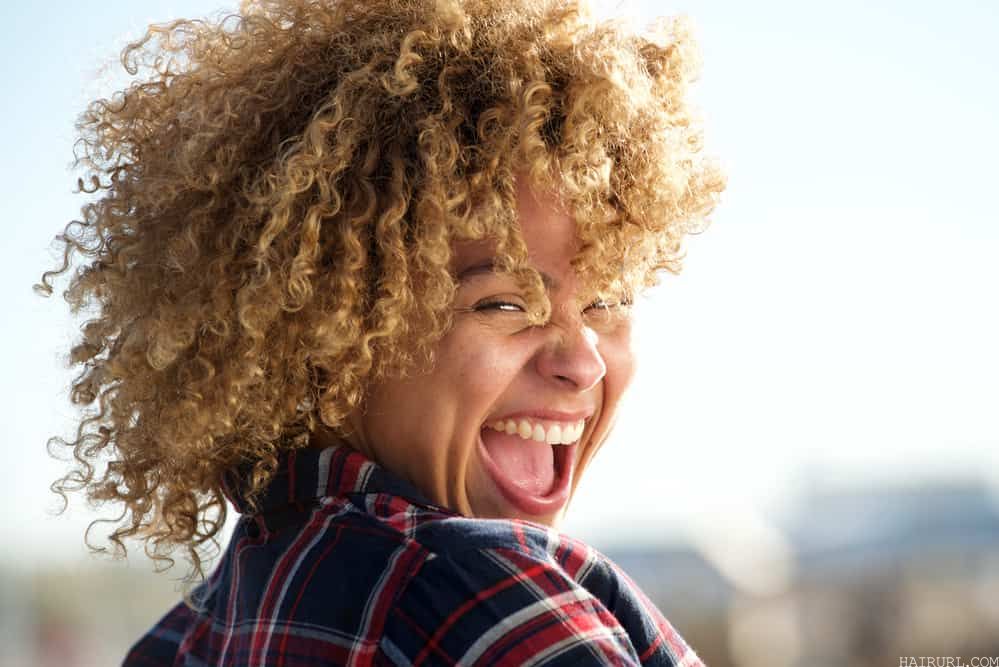 Cute African American female with blonde hair and orange tones laughing outdoors