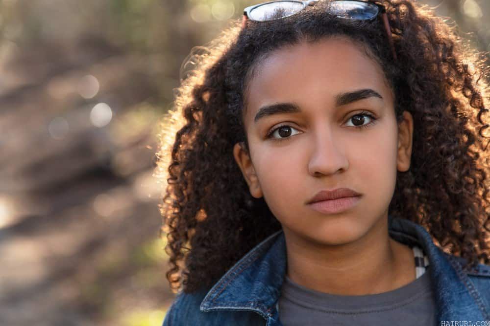 Outdoor portrait of beautiful mixed race teenager female looking thoughtful with curly hair. 