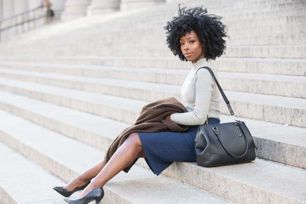 African American female wearing a ribbed sweater, blue skirt, black heals and with beautiful curly hair.