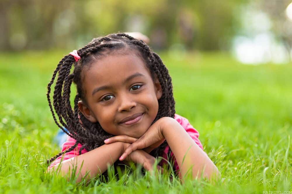 Young girl with an adorable hairstyle with braids all around while lying down on the grass