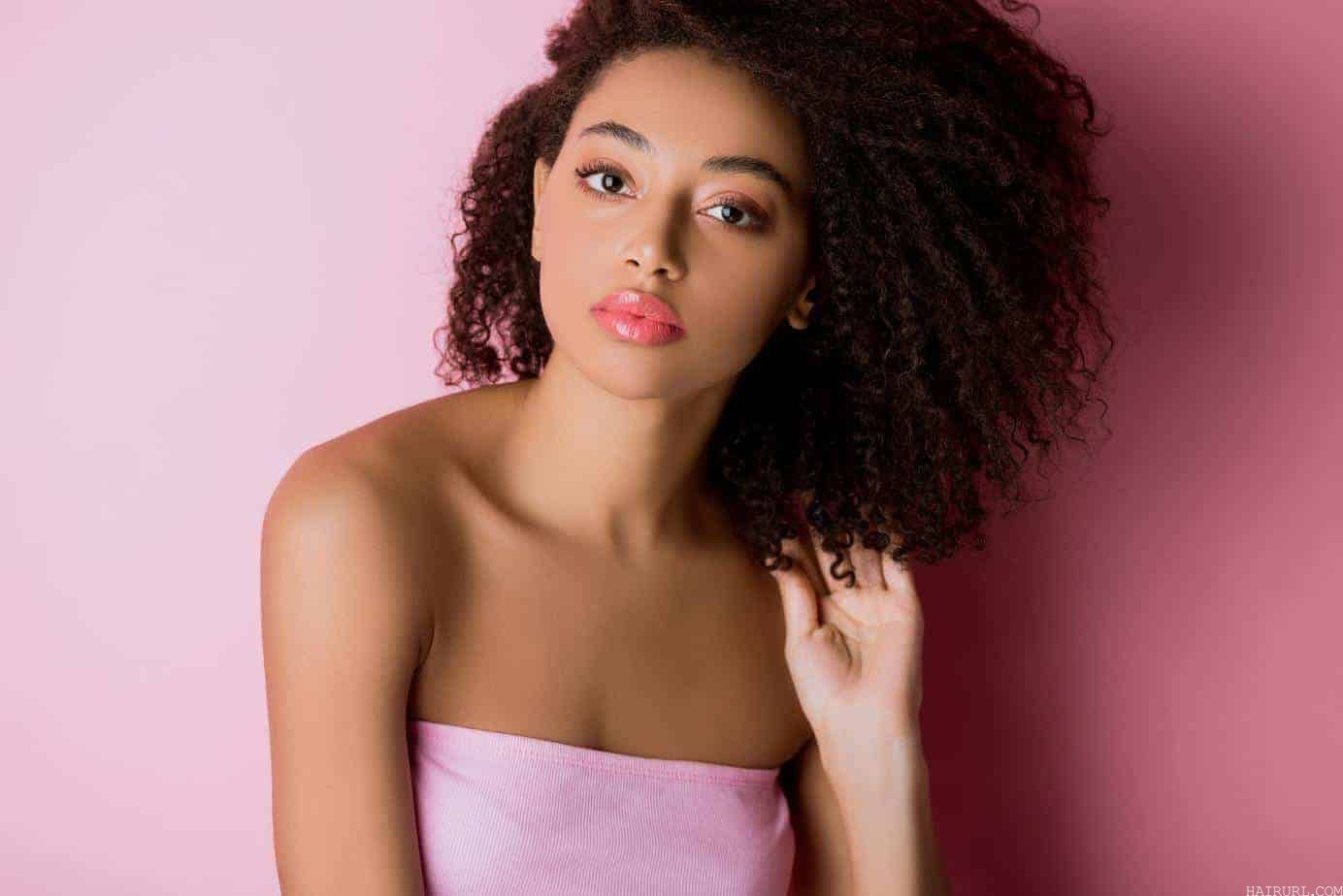 stunning African American female wearing a pink dress, matching lipstick and a gorgeous curly hairstyle