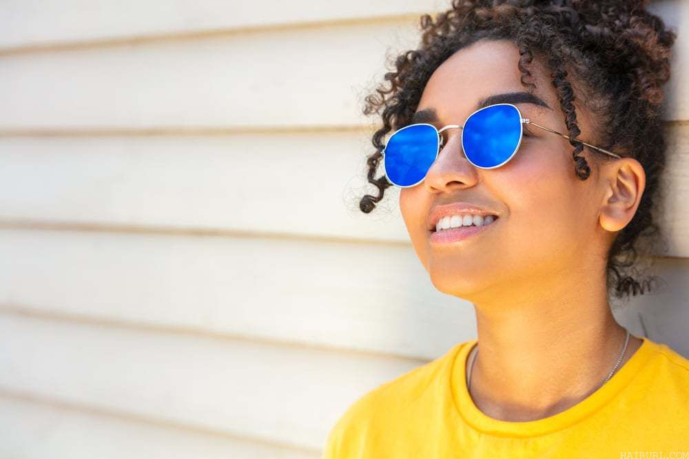 Cute girl with coconut oil treated hair wearing blue sunglasses and a yellow t-shirt on vacation smiling in summer sunshine.