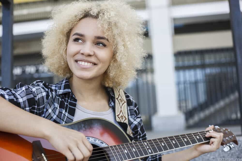 African American girl with ash blonde hair dye playing the guitar outside