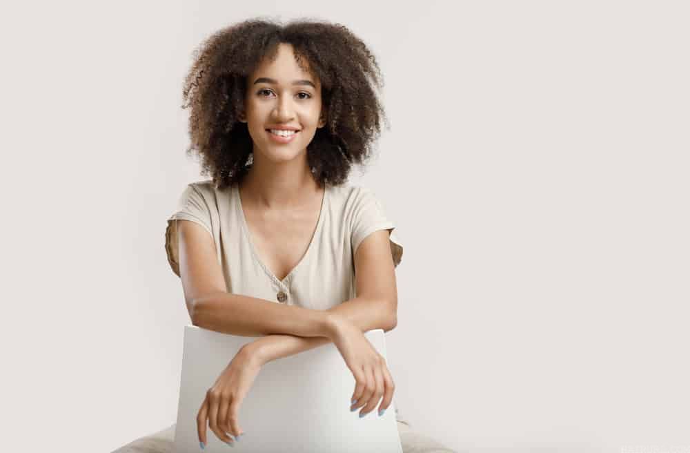 Young African American blogger with naturally curly hair sitting on a white chair 
