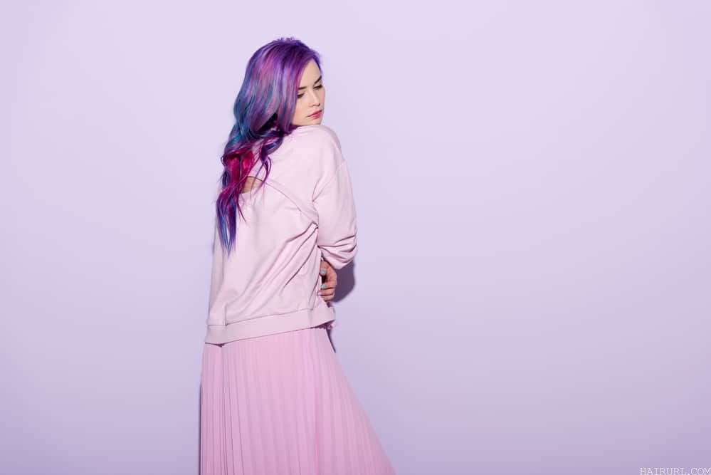 Female wearing a pink sweater and skirt with a dark purple faded hair color with a blue undertone.