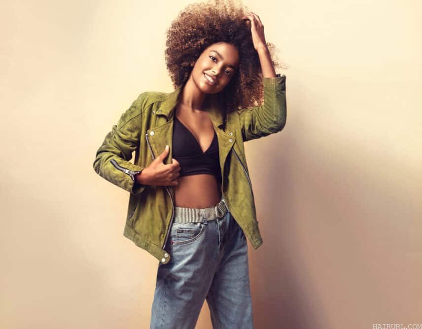 African American women wearing a green jacket, black shirt, blue jeans, and naturally curly brown hair strands.