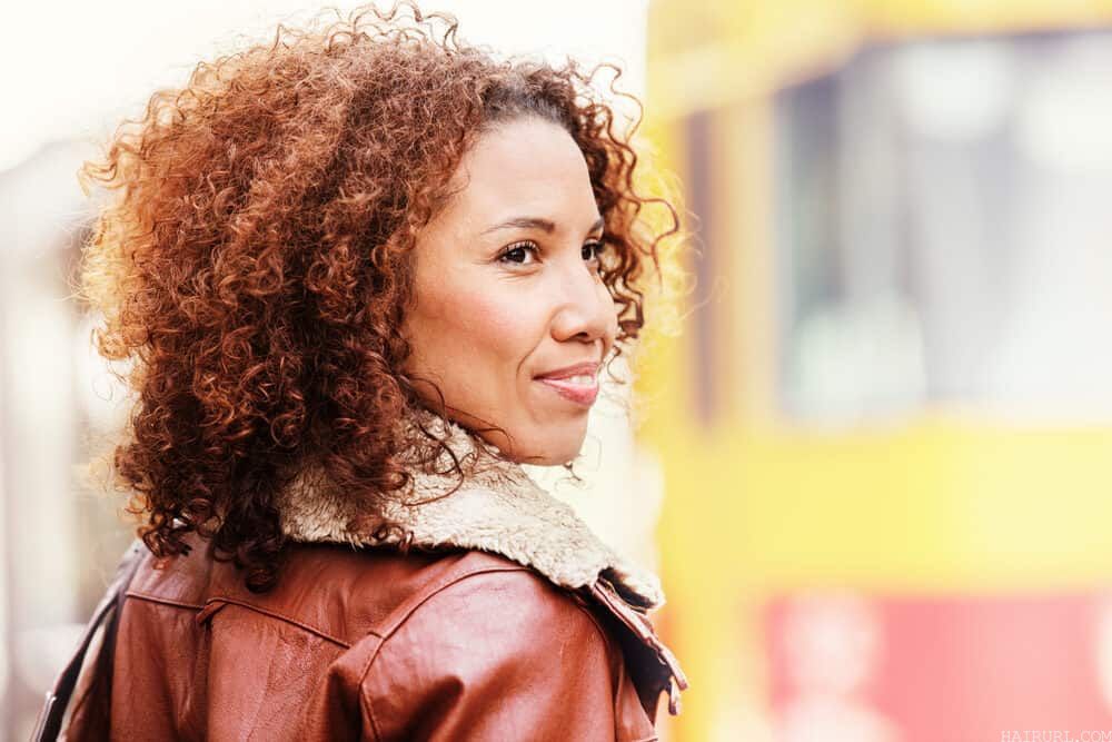 Black girl with hair bleached red and brown while wearing a red and brown jacket.