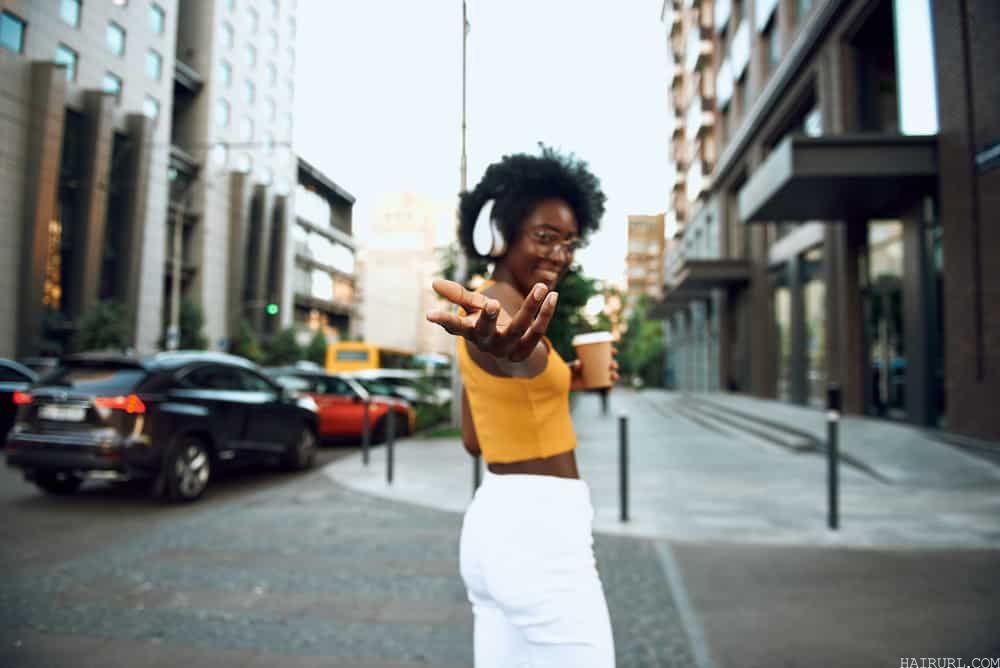 Cute black girl with naturally wavy hair wearing a yellow shirt and white pants.
