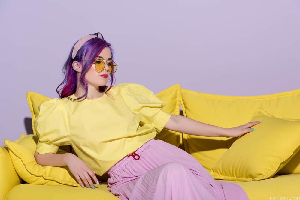 Caucasian women with faded Fuschia hair strands wearing a shirt with a bleach yellow tone and a pink ribbed skirt.