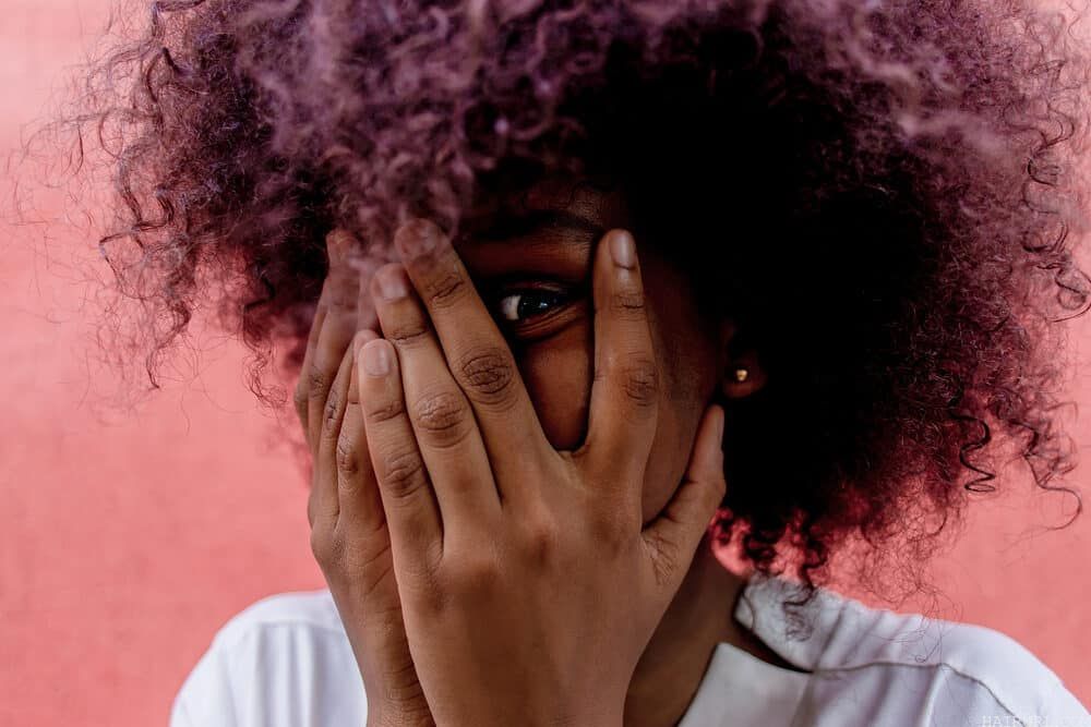 African American female with freshly washed hair covers face with hands.