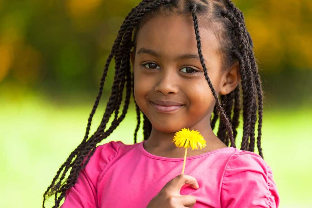 Cute African American girl holding a dandelion flower showing off her natural beauty with the perfect hairstyle