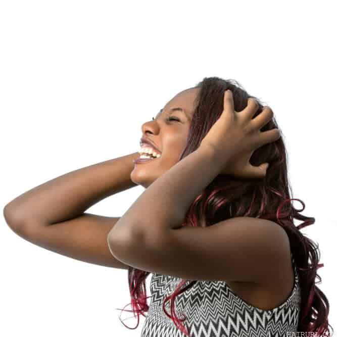 Black woman laughing as she holds her kool-aid dyed hair strands.