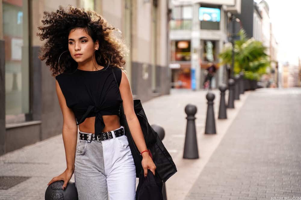 Young Colombian female with a unique style wearing large hoop earrings, a black t-shirt, and gray and white jeans.